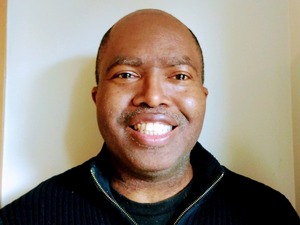 professor in a black zip up sweater in front of a white backdrop